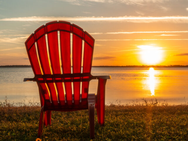 Empty chair facing a sunset on a quiet lake, symbolizing reflection, solitude, and the longing for connection in a divided world.